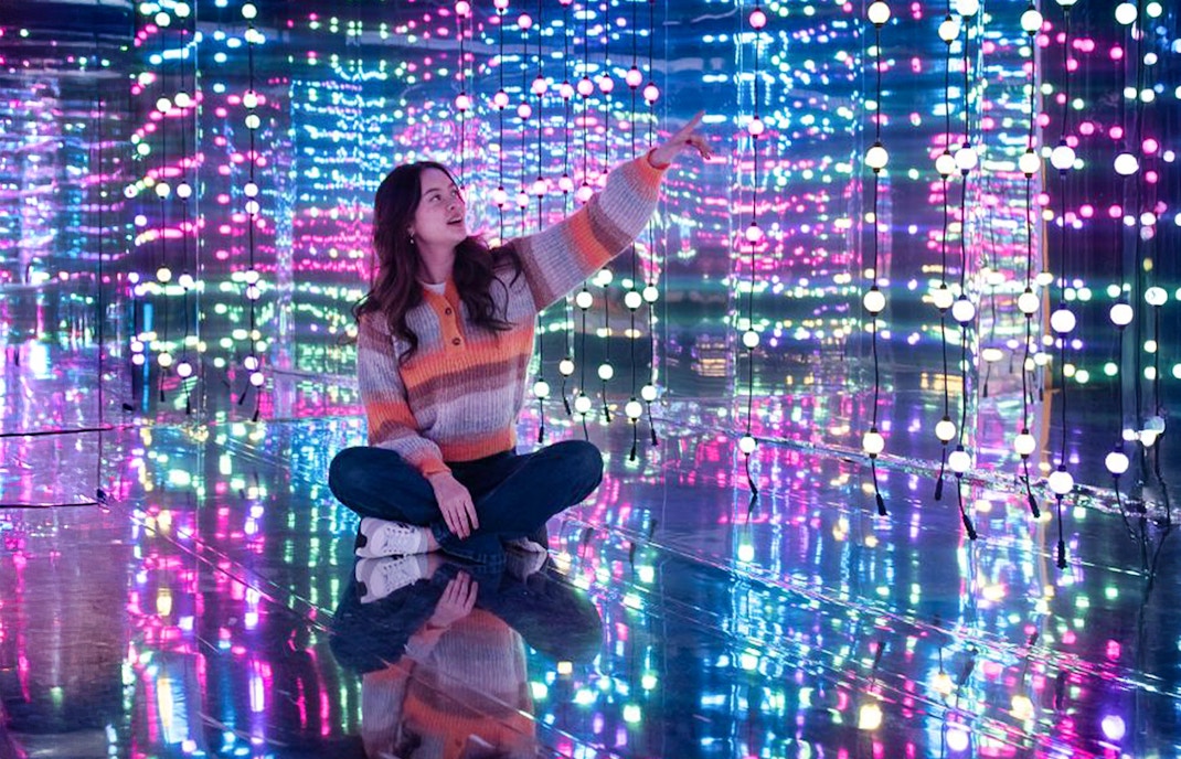 Person sitting in a mirrored room with colorful lights at Dopamine Land, Washington D.C.