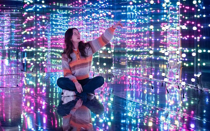 Person sitting in a mirrored room with colorful lights at Dopamine Land, Washington D.C.
