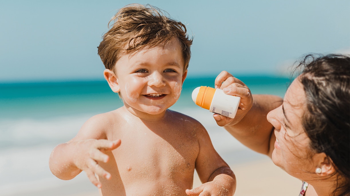 Child on beach applying sunscreen, highlighting travel tip to carry sunscreen.