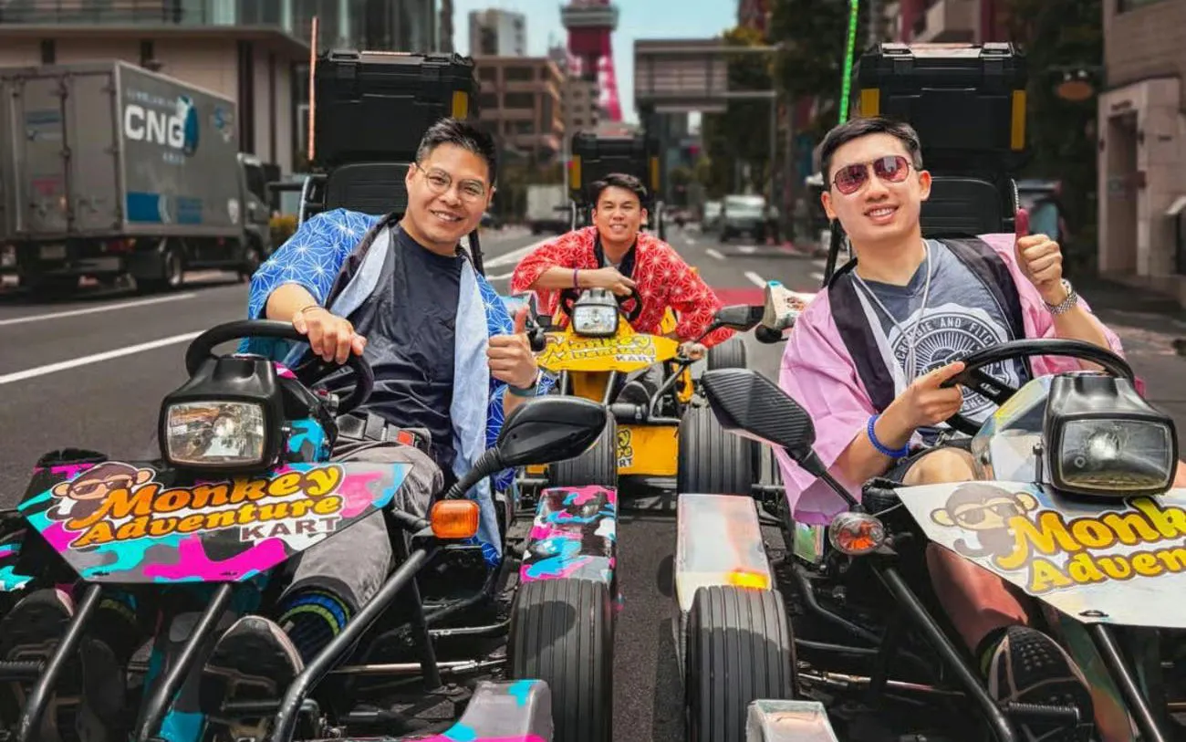 Go-kart riders in colorful outfits on a Tokyo street with Tokyo Tower in the background.