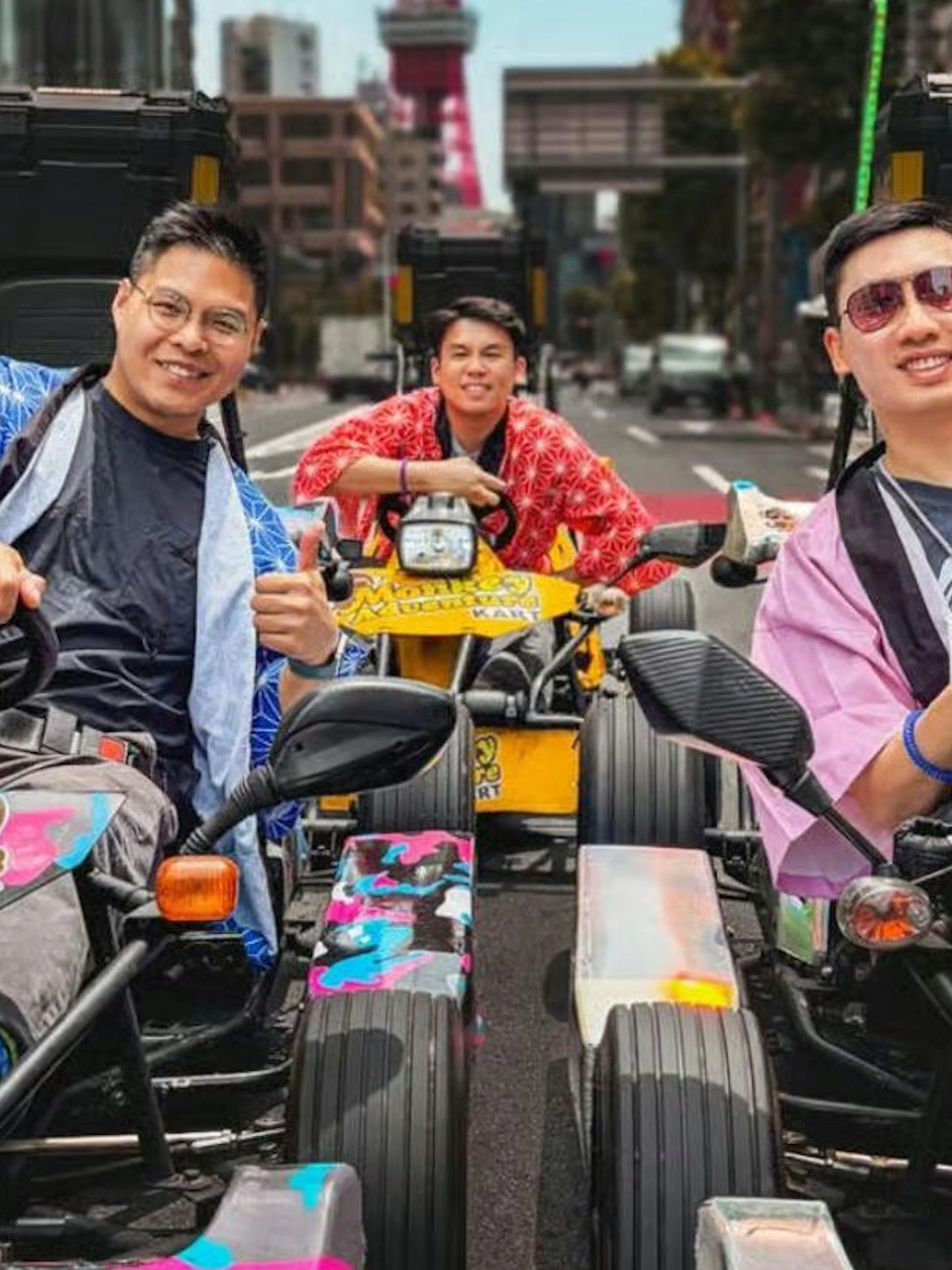 Go-kart riders in colorful outfits on a Tokyo street with Tokyo Tower in the background.