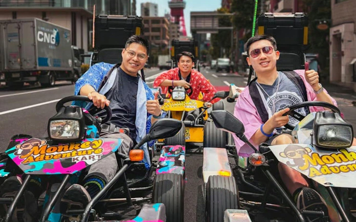 Go-kart riders in colorful outfits on a Tokyo street with Tokyo Tower in the background.