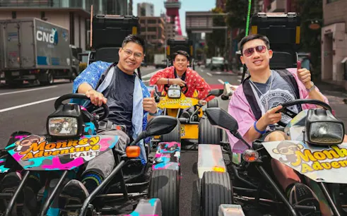 Go-kart riders in colorful outfits on a Tokyo street with Tokyo Tower in the background.