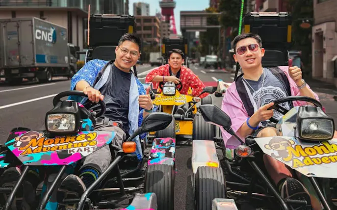 Go-kart riders in colorful outfits on a Tokyo street with Tokyo Tower in the background.