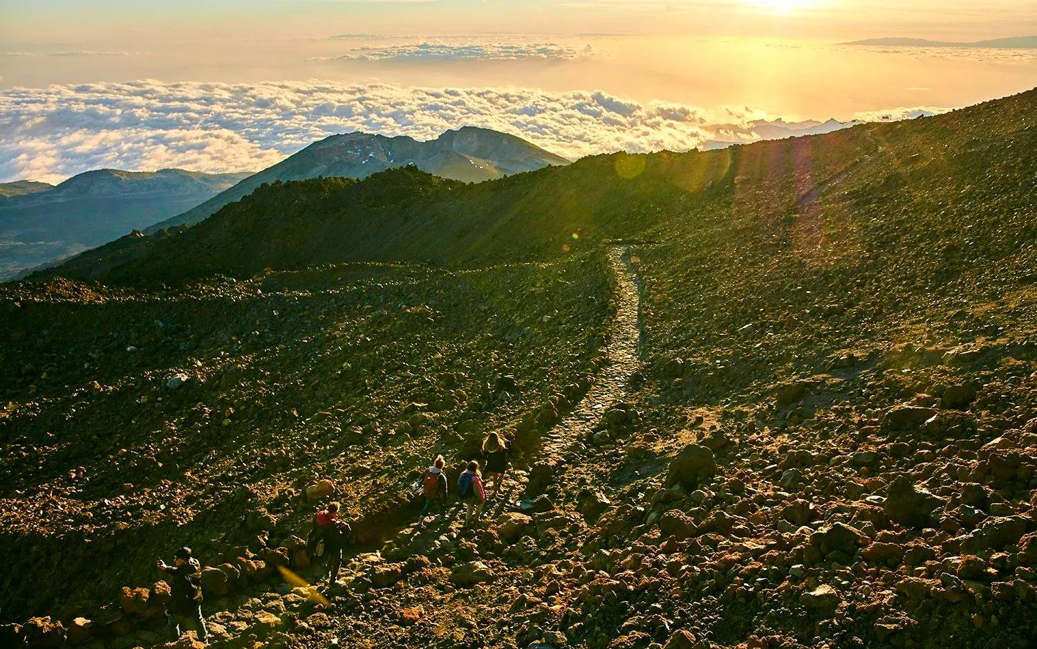 Hikers on rocky path at sunset on Mount Teide, Tenerife.