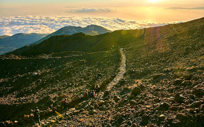 Hikers on rocky path at sunset on Mount Teide, Tenerife.