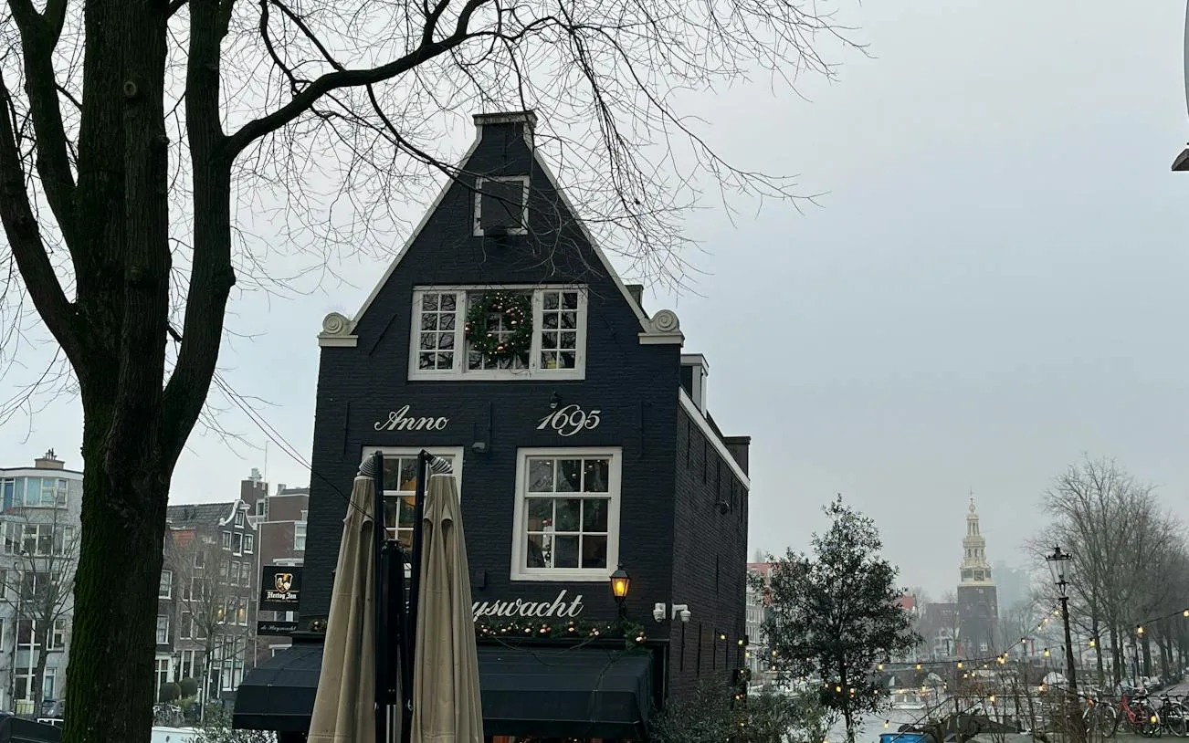 Historic Amsterdam building with "Anno 1695" facade near canal, part of Rembrandt's Lost Painting city exploration game.