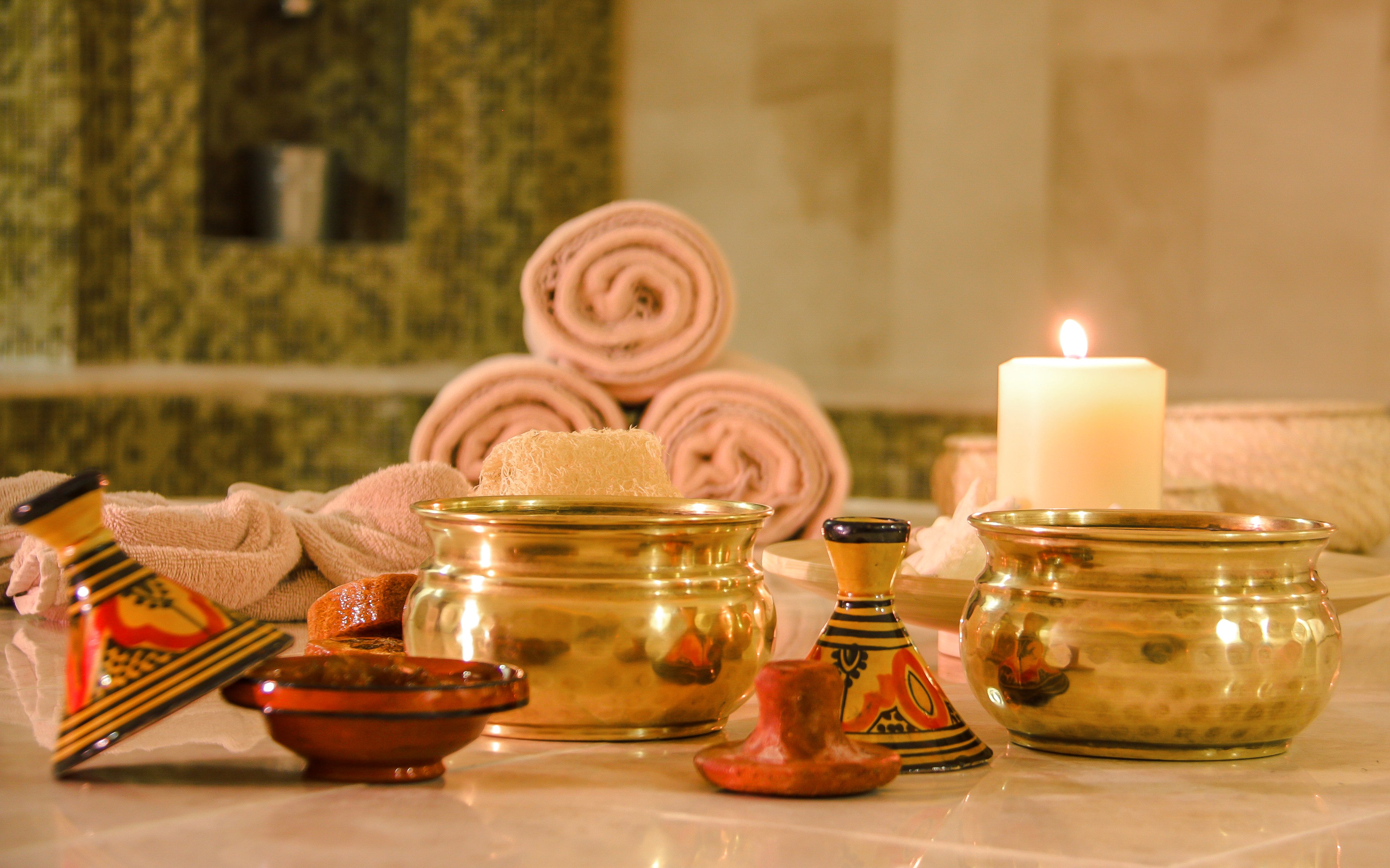 Rolled towels and brass bowls in a Turkish bath setting with a lit candle.