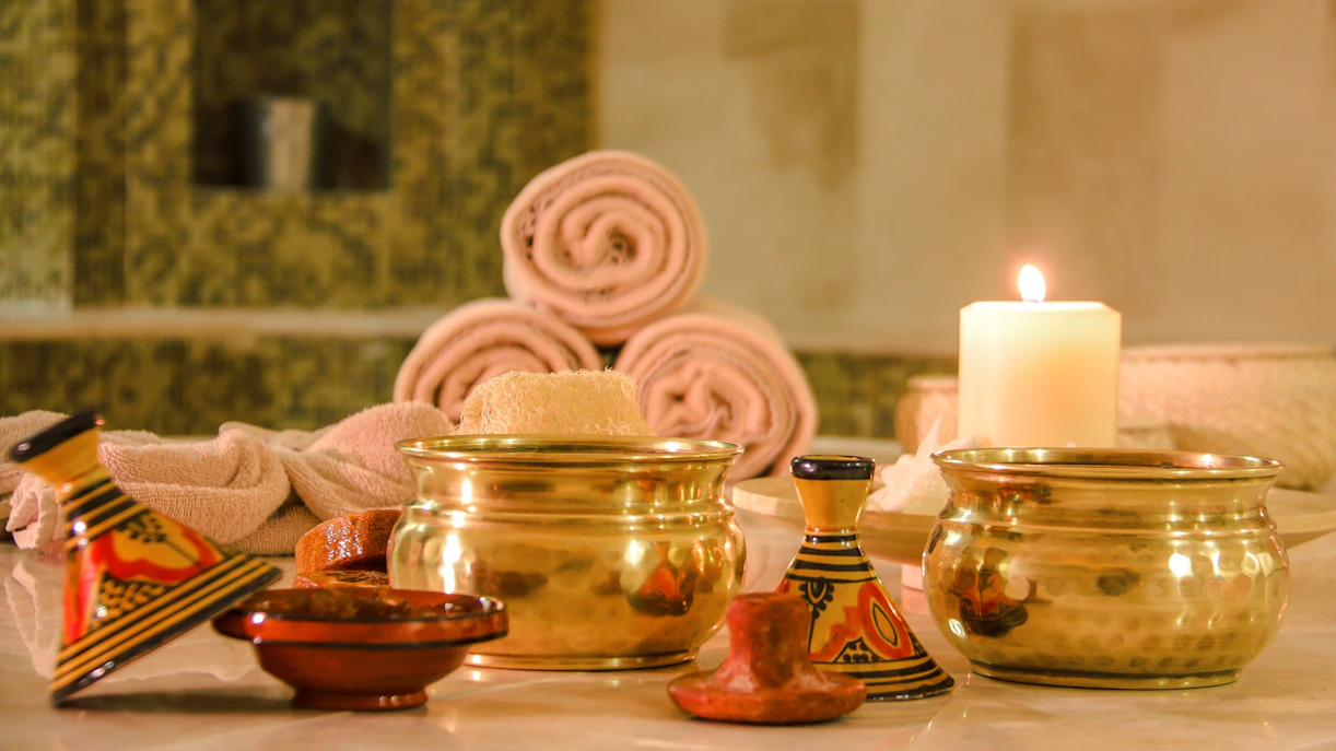 Rolled towels and brass bowls in a Turkish bath setting with a lit candle.