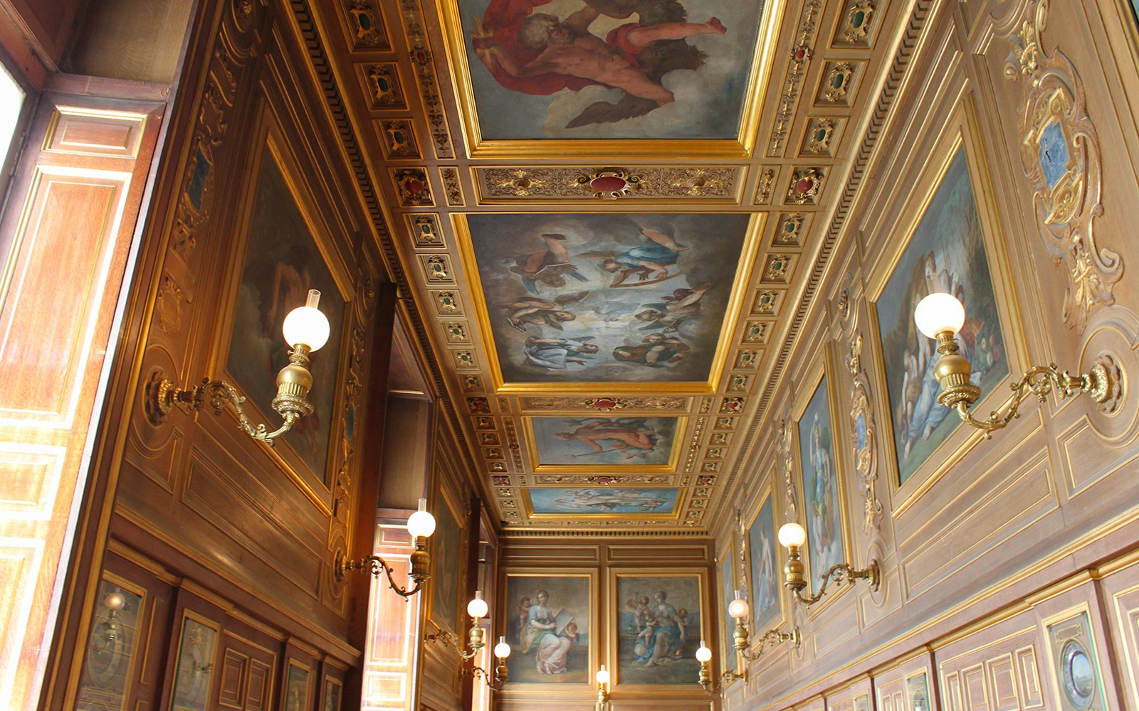 Château de Fontainebleau ornate hallway with detailed ceiling paintings and wall sconces.