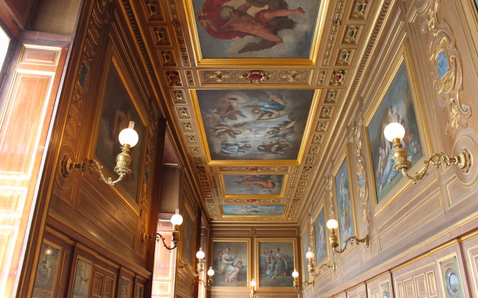 Château de Fontainebleau ornate hallway with detailed ceiling paintings and wall sconces.