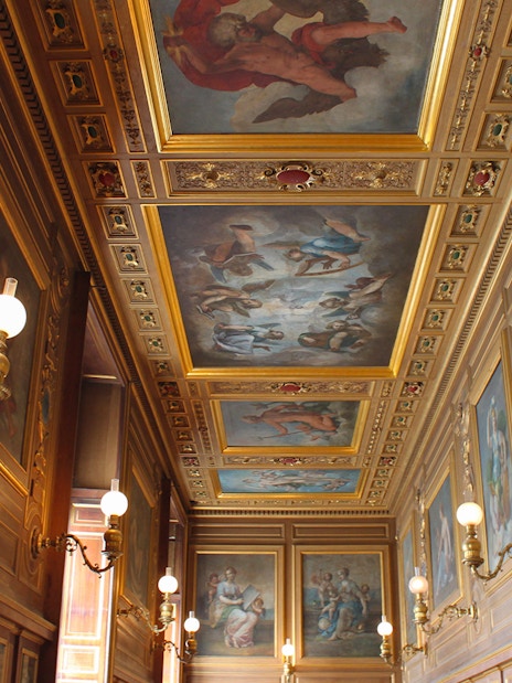 Château de Fontainebleau ornate hallway with detailed ceiling paintings and wall sconces.