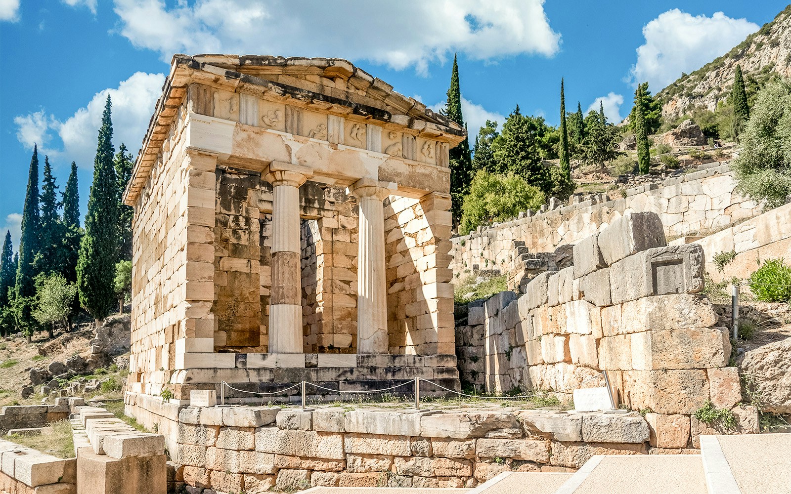 Athenian Treasury at Delphi Archaeological Site with stone columns and ancient ruins.