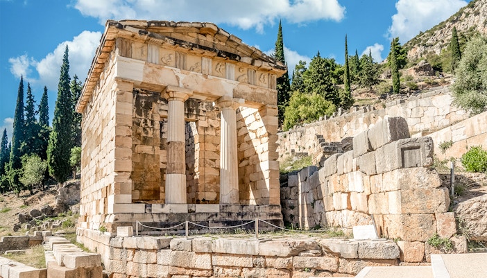 Athenian Treasury at Delphi Archaeological Site with stone columns and ancient ruins.