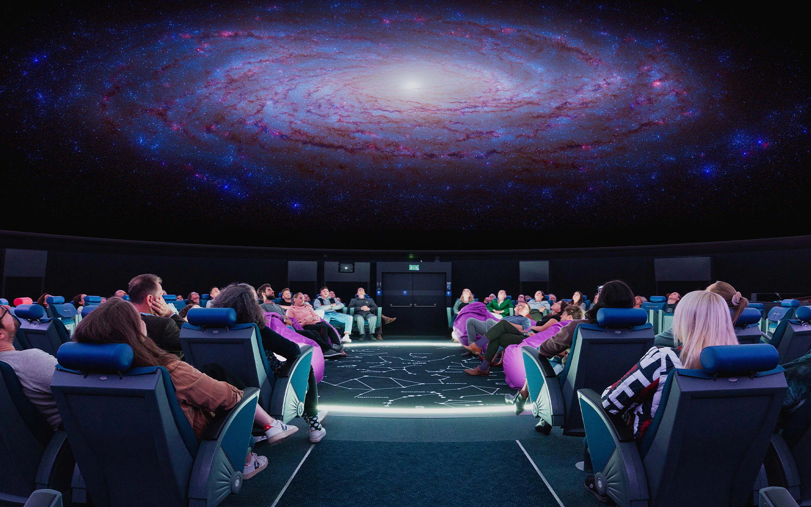 Visitors seated in the Swiss Museum of Transport planetarium viewing a galaxy projection.