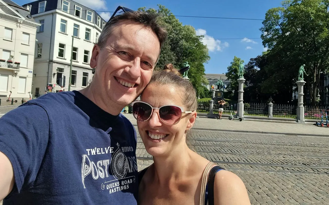 Couple enjoying a sunny day in front of statues at a historical site in Brussels.