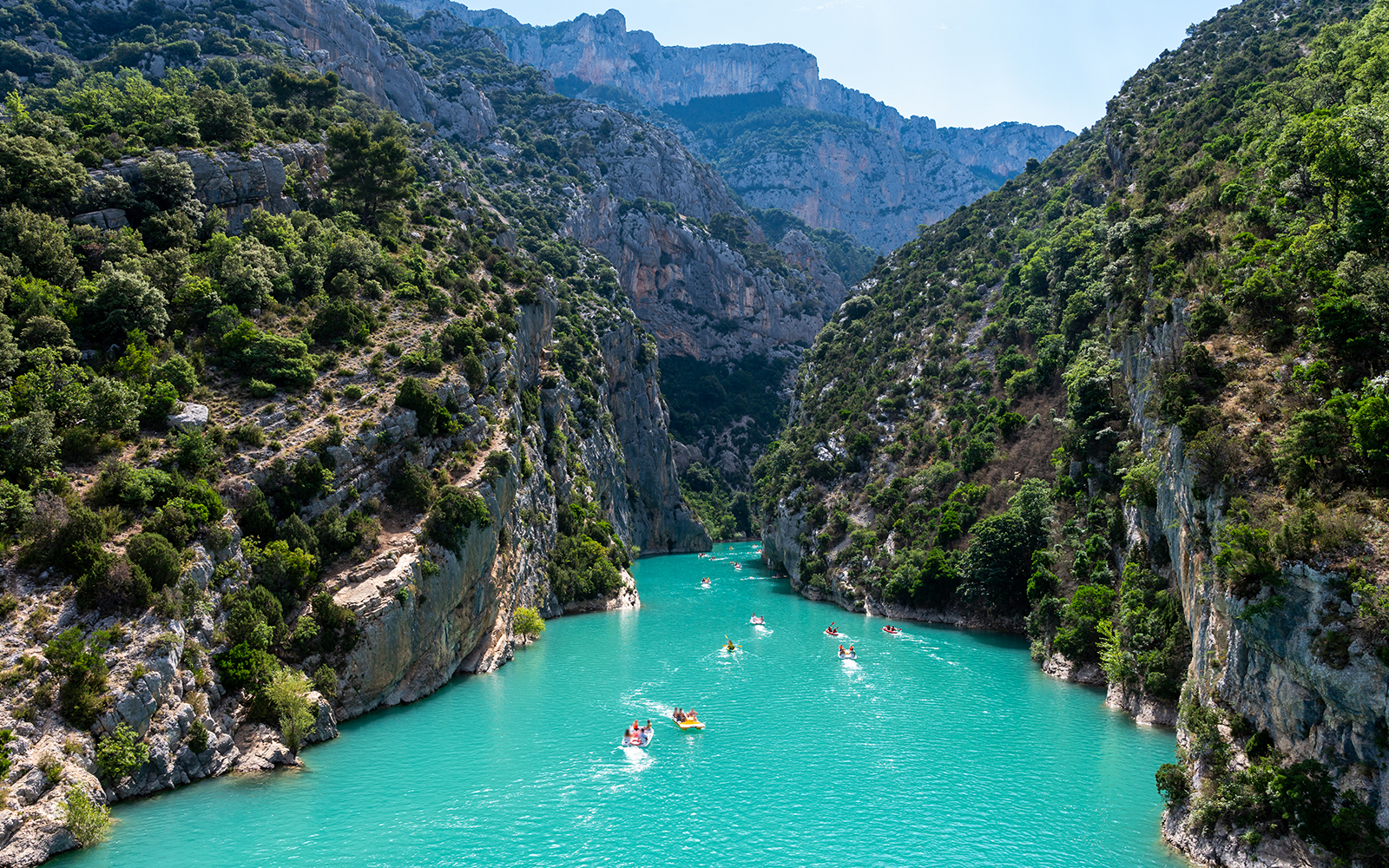 Kayakers on turquoise waters of Gorges du Verdon, surrounded by steep cliffs and lush greenery.