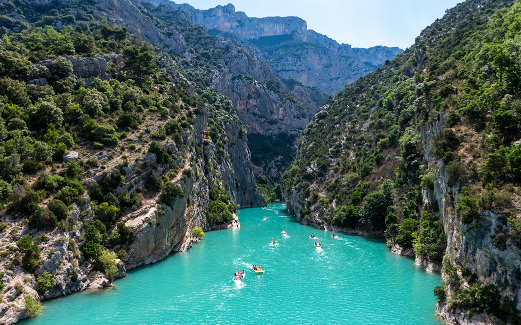 Kayakers on turquoise waters of Gorges du Verdon, surrounded by steep cliffs and lush greenery.