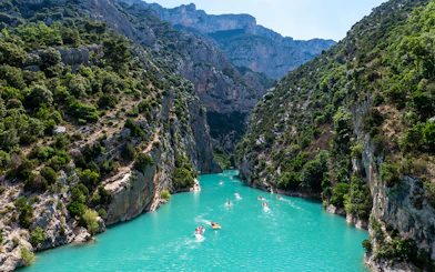 Kayakers on turquoise waters of Gorges du Verdon, surrounded by steep cliffs and lush greenery.