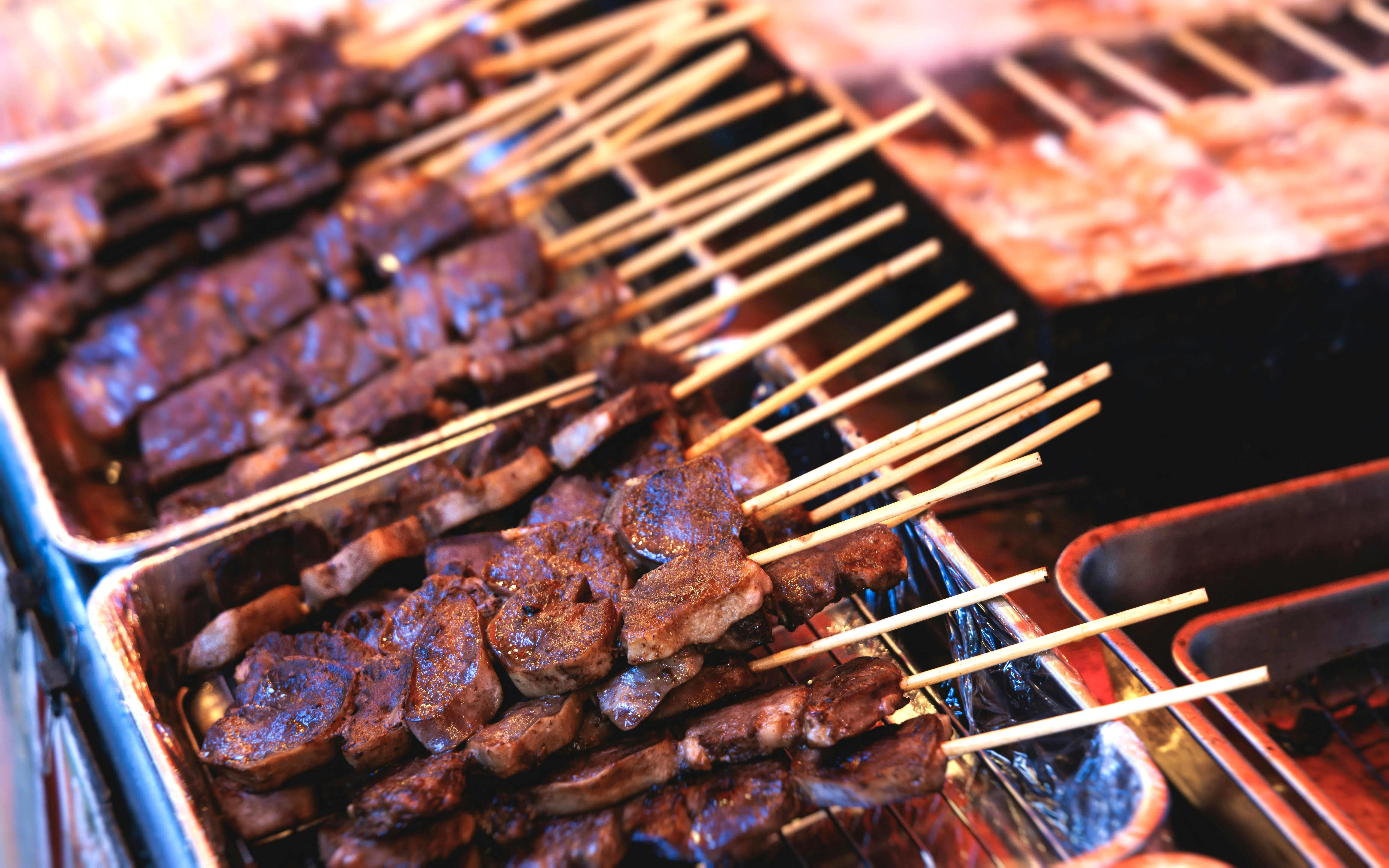 Wagyu beef skewers grilling on teppanyaki plate at Tokyo street food festival.