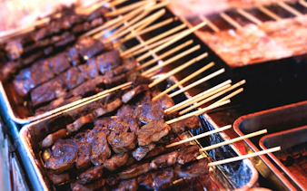 Wagyu beef skewers grilling on teppanyaki plate at Tokyo street food festival.
