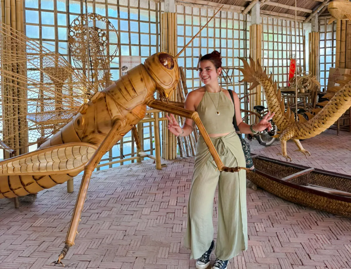 Woman interacting with large bamboo grasshopper sculpture in Hoi An craft workshop.