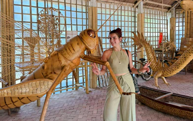 Woman interacting with large bamboo grasshopper sculpture in Hoi An craft workshop.