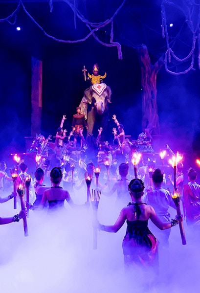 Performers with torches surround an elephant and rider on stage at Phuket Fantasea show.