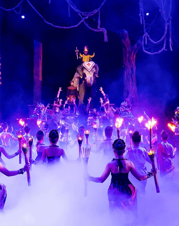 Performers with torches surround an elephant and rider on stage at Phuket Fantasea show.