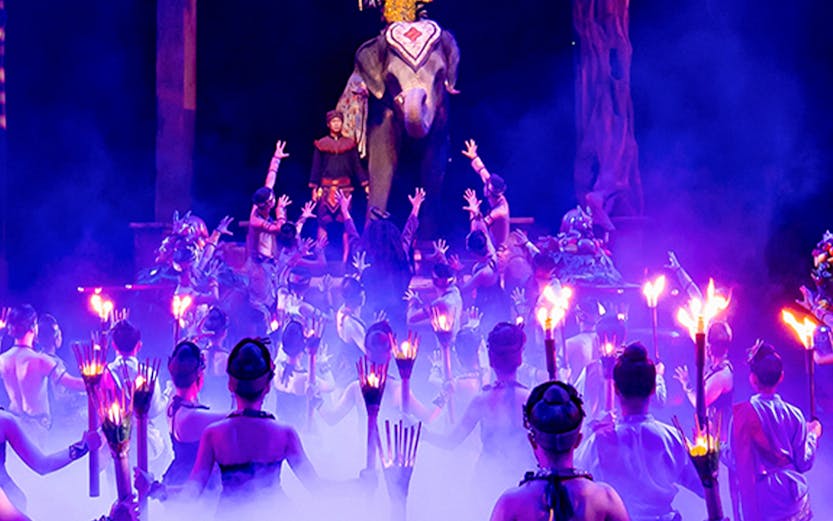 Performers with torches surround an elephant and rider on stage at Phuket Fantasea show.