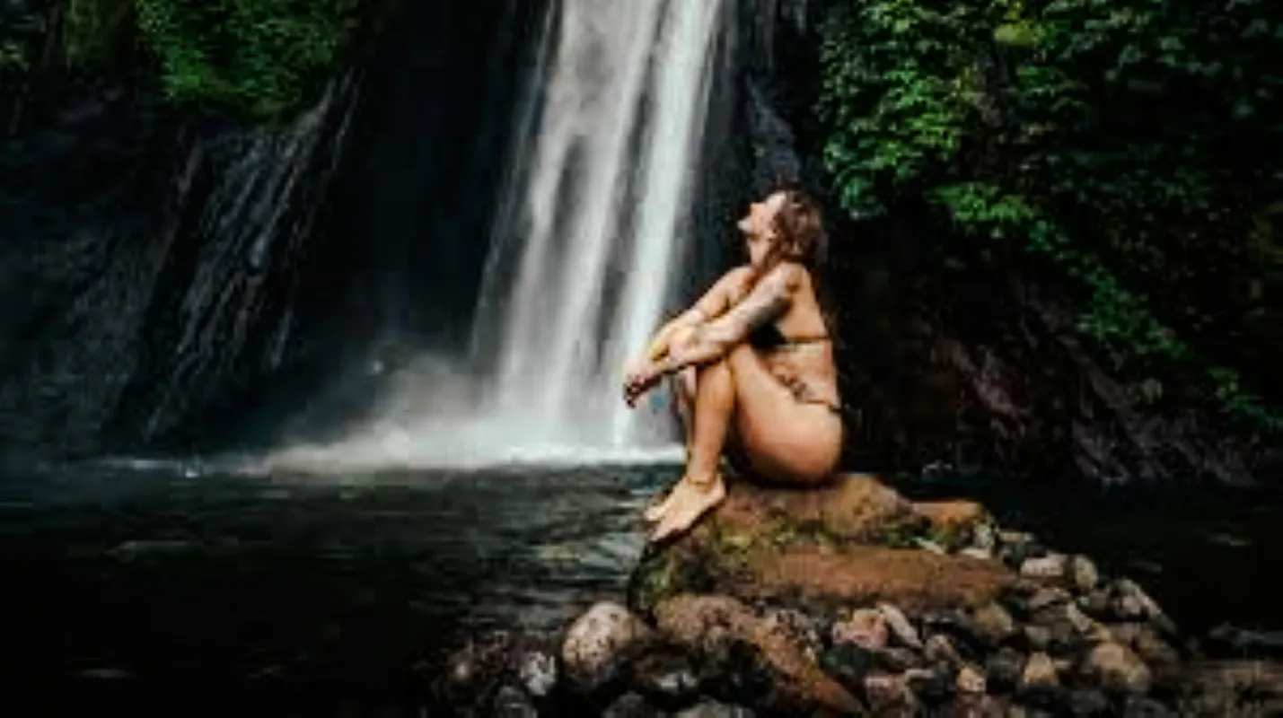 Person sitting on rocks by Sekumpul Waterfalls, Bali.