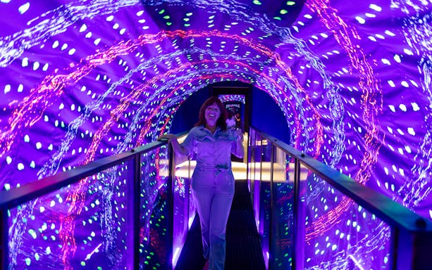 Guest walking through a vibrant light tunnel at the Museum of Illusions Amsterdam.
