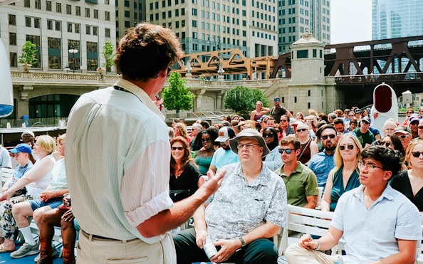 Tour guide speaking to a group on a Chicago River Architecture Tour with city buildings in the background.