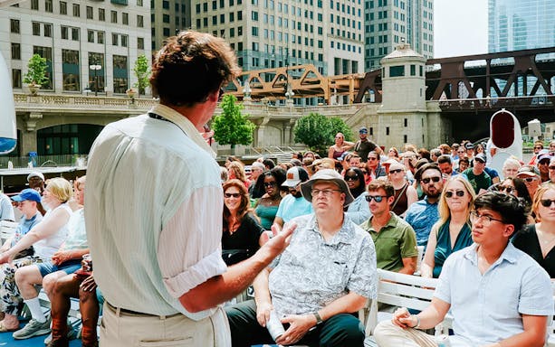 Tour guide speaking to a group on a Chicago River Architecture Tour with city buildings in the background.