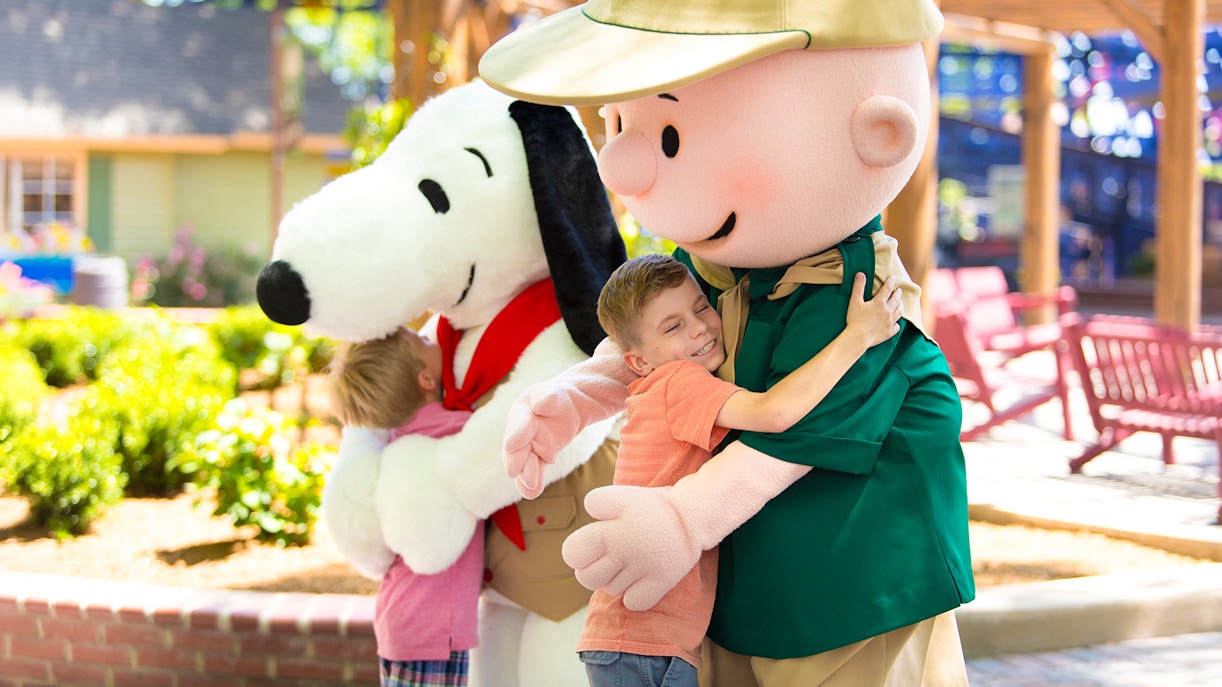 Children hugging Snoopy and a character at Six Flags Carowinds, CAMP SNOOPY®.
