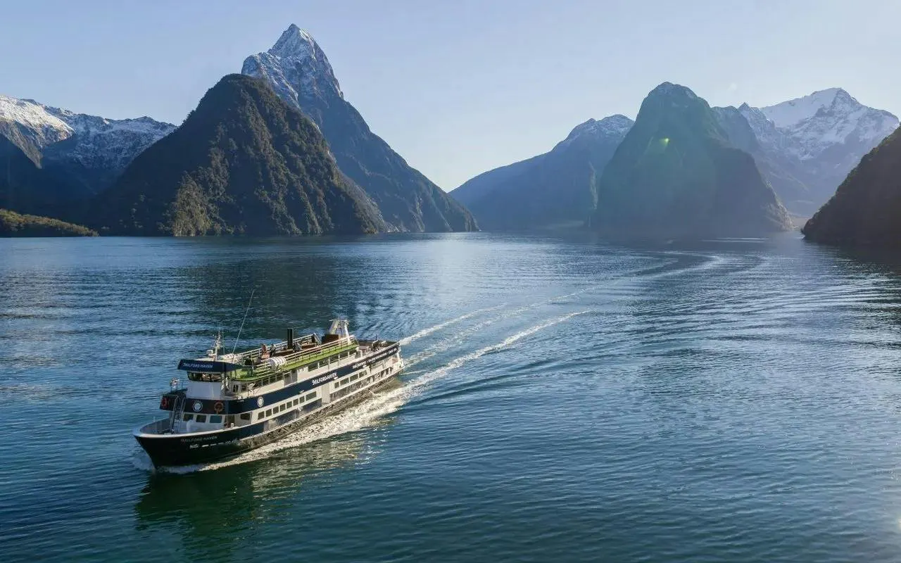 Cruise ship sailing through Milford Sound with mountain peaks, Te Anau departure.