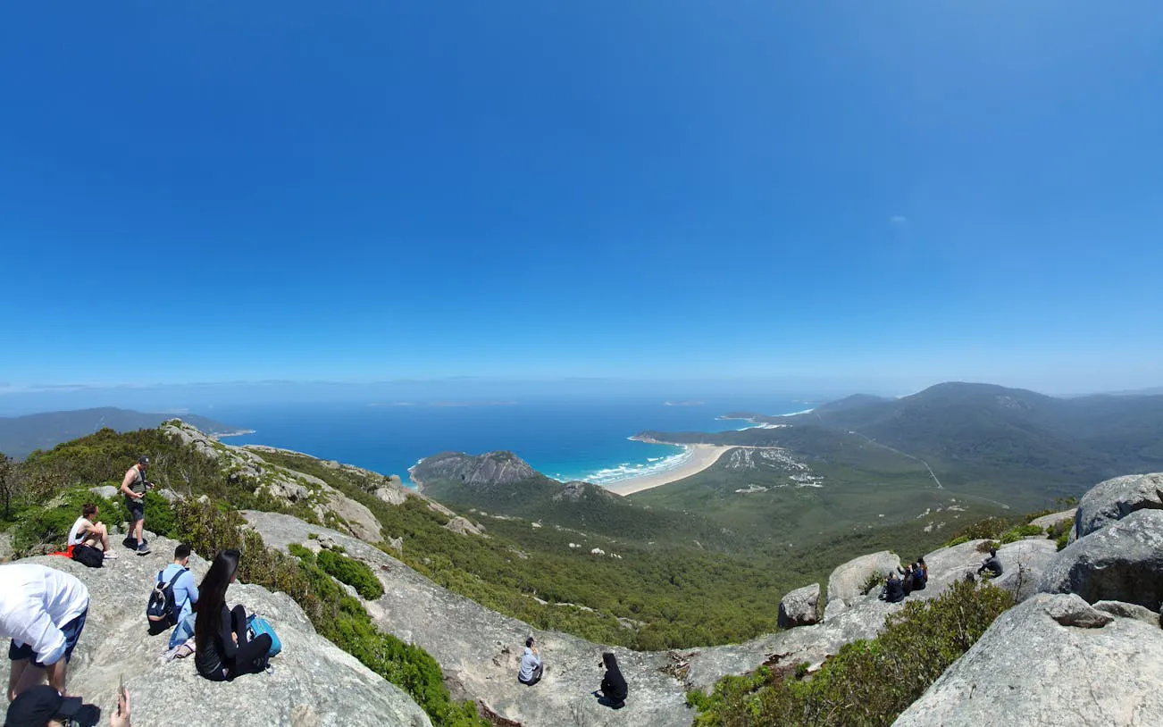 Hikers enjoying the view from Mount Oberon at Wilsons Promontory National Park, overlooking Tidal River and Squeaky Beach.