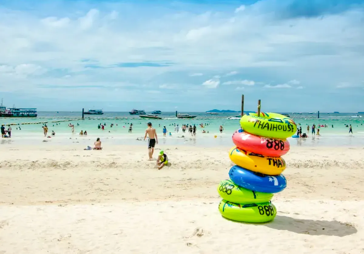Beachgoers enjoy Pattaya's Coral Island with colorful inflatables and speedboats in the background.