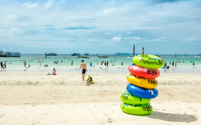 Beachgoers enjoy Pattaya's Coral Island with colorful inflatables and speedboats in the background.