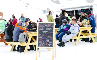 Visitors enjoying outdoor seating at Farellones Park with a menu board, Santiago.