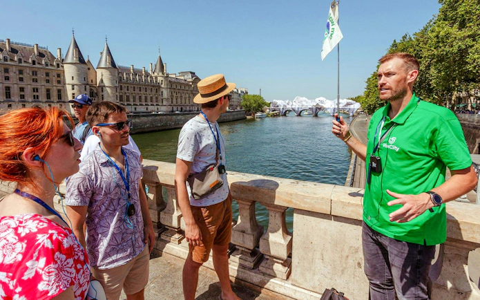Tour guide leading a group near the Seine River with Conciergerie in the background, Paris.