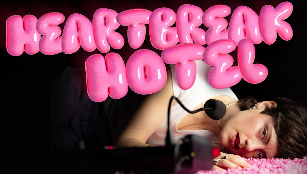 Person lying on pink carpet with microphone, "Heartbreak Hotel" in bold pink letters above.