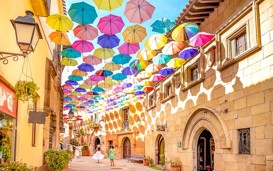 Tourists walking under colorful umbrellas in Poble Espanyol, Barcelona.