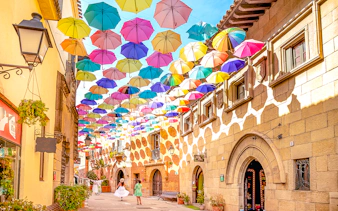 Tourists walking under colorful umbrellas in Poble Espanyol, Barcelona.