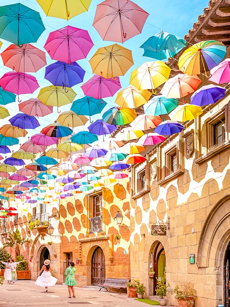 Tourists walking under colorful umbrellas in Poble Espanyol, Barcelona.