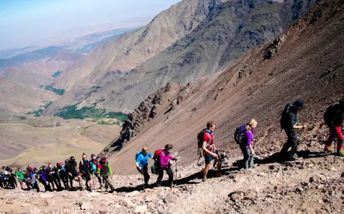 Hikers ascending rocky trail in Marrakesh mountains.