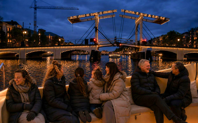 People enjoying a boat tour during the Amsterdam Light Festival with illuminated bridge in view.