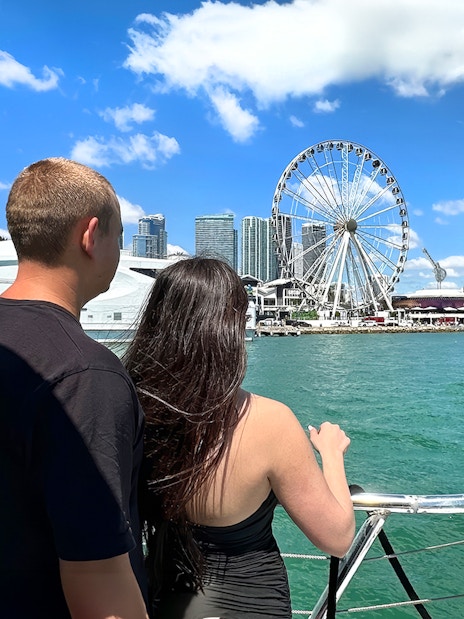 Couple on boat with Miami skyline and Ferris wheel in view.