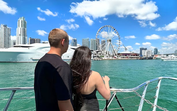 Couple on boat with Miami skyline and Ferris wheel in view.