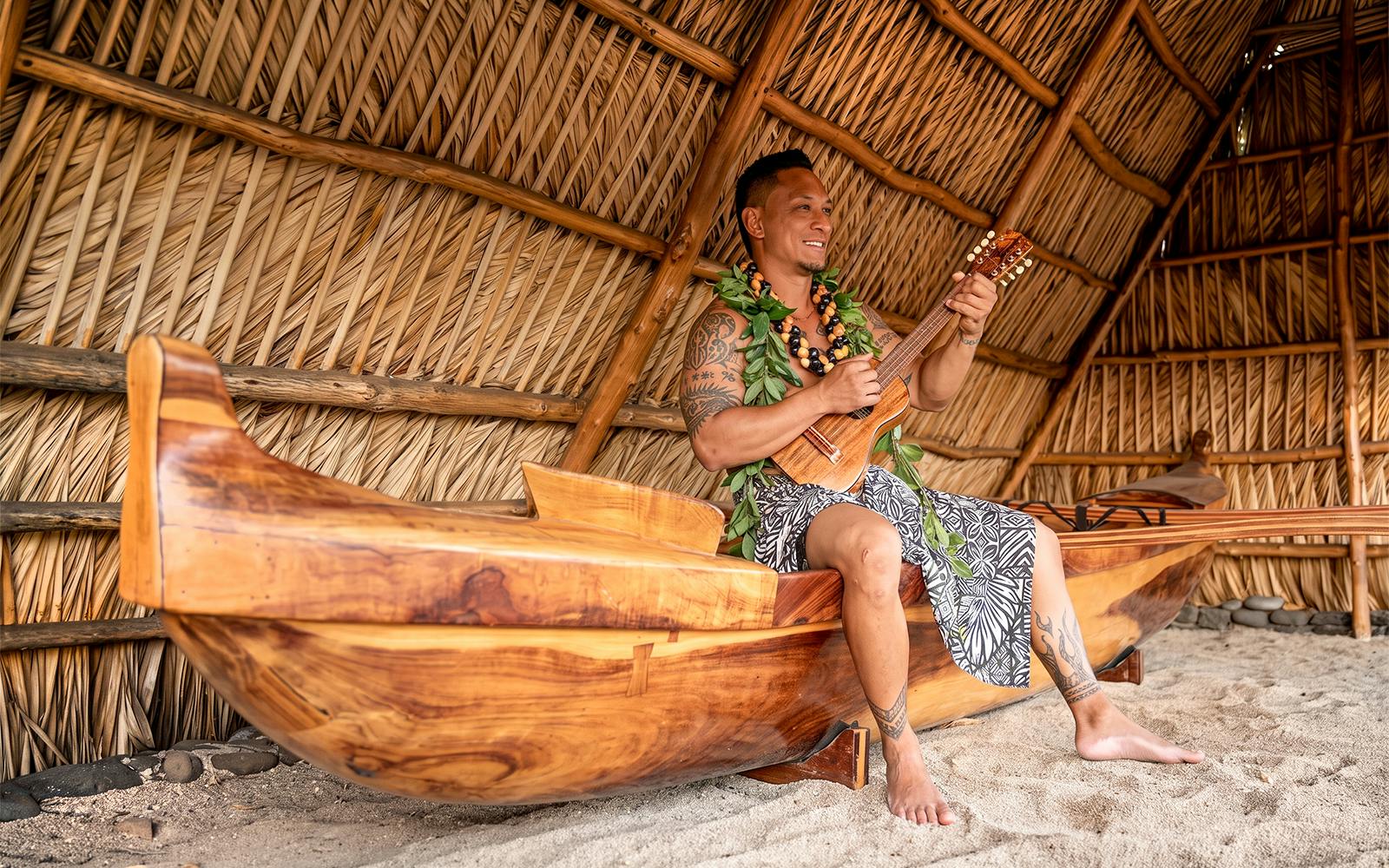 Man playing ukulele in traditional Hawaiian hut at Old Lahaina Luau.